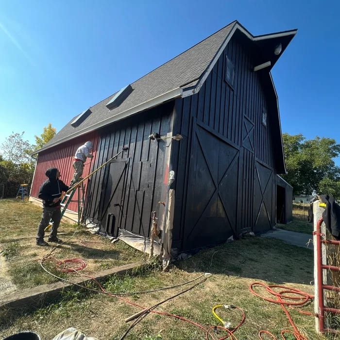 QC Painting crew spraying a gambrel barn from red to black during an exterior repaint