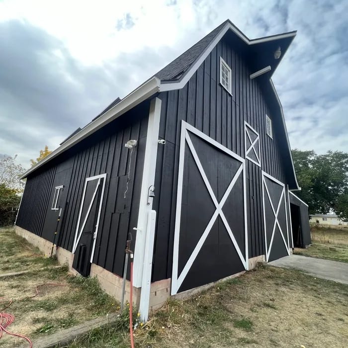 Side elevation of a black barn with white trim and attached lean-to after exterior painting