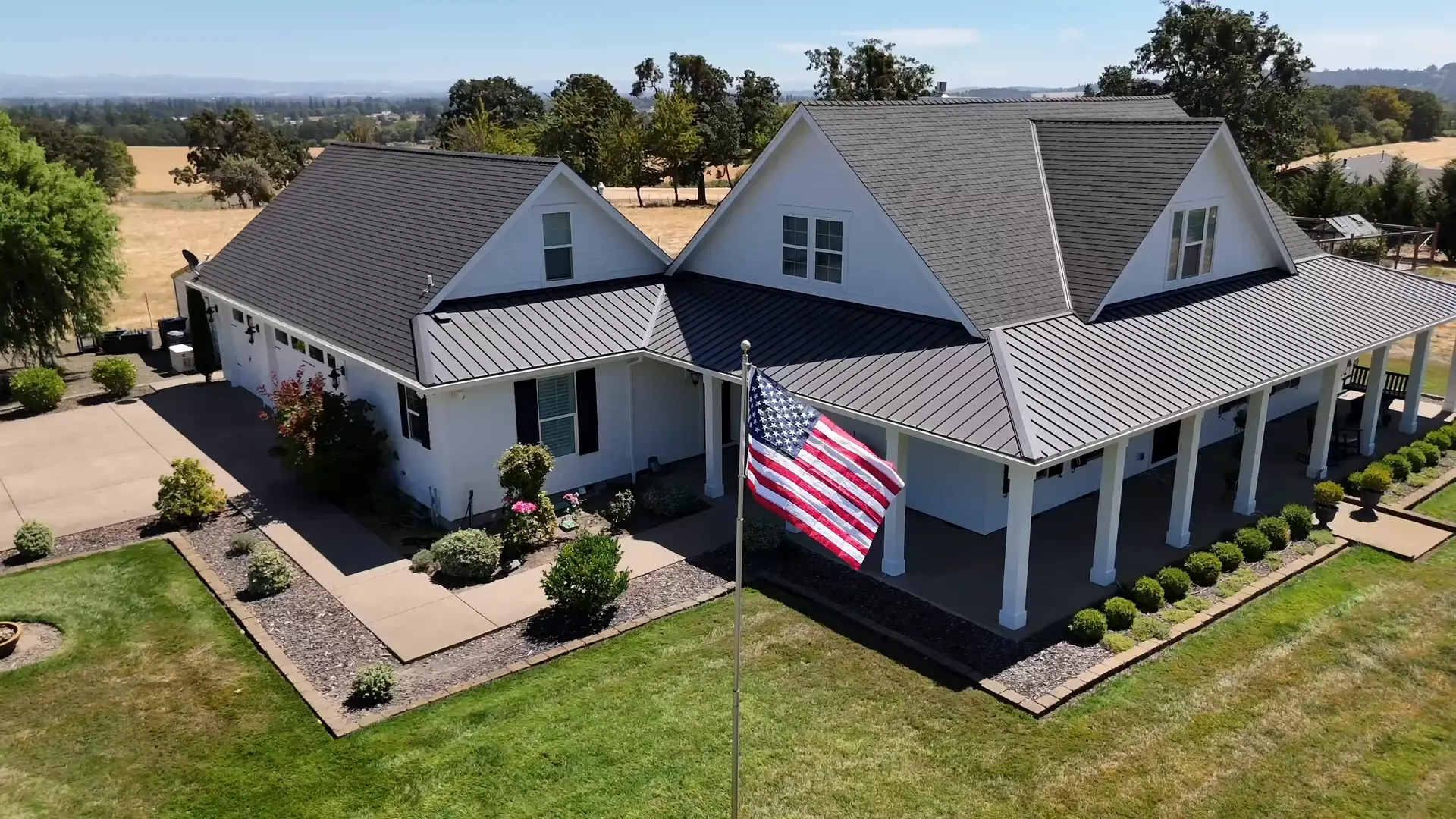 White farmhouse with a wraparound porch, black shutters and a metal porch roof