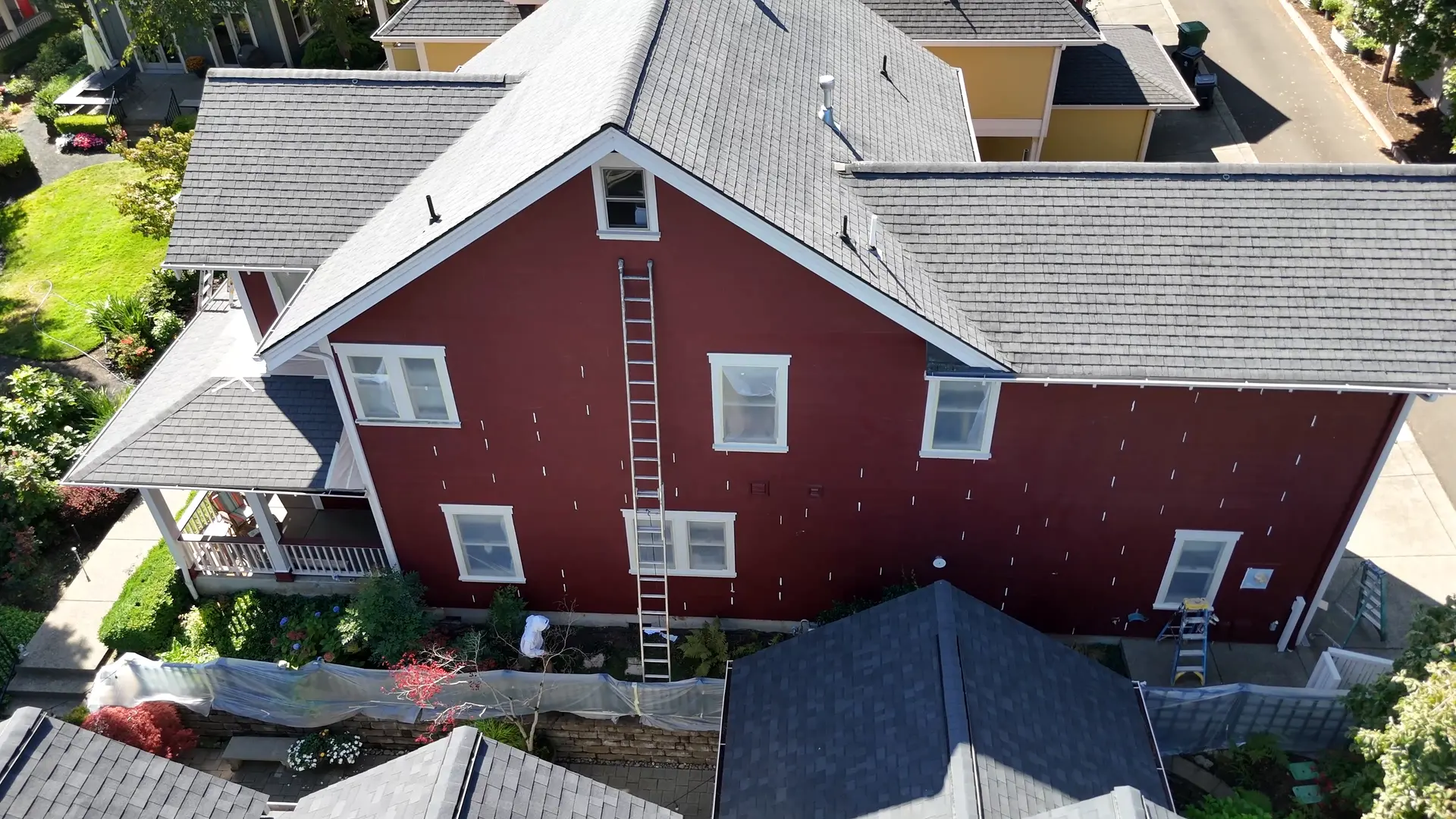 Side of the Craftsman during prep, faded red siding with spot primer and ladders