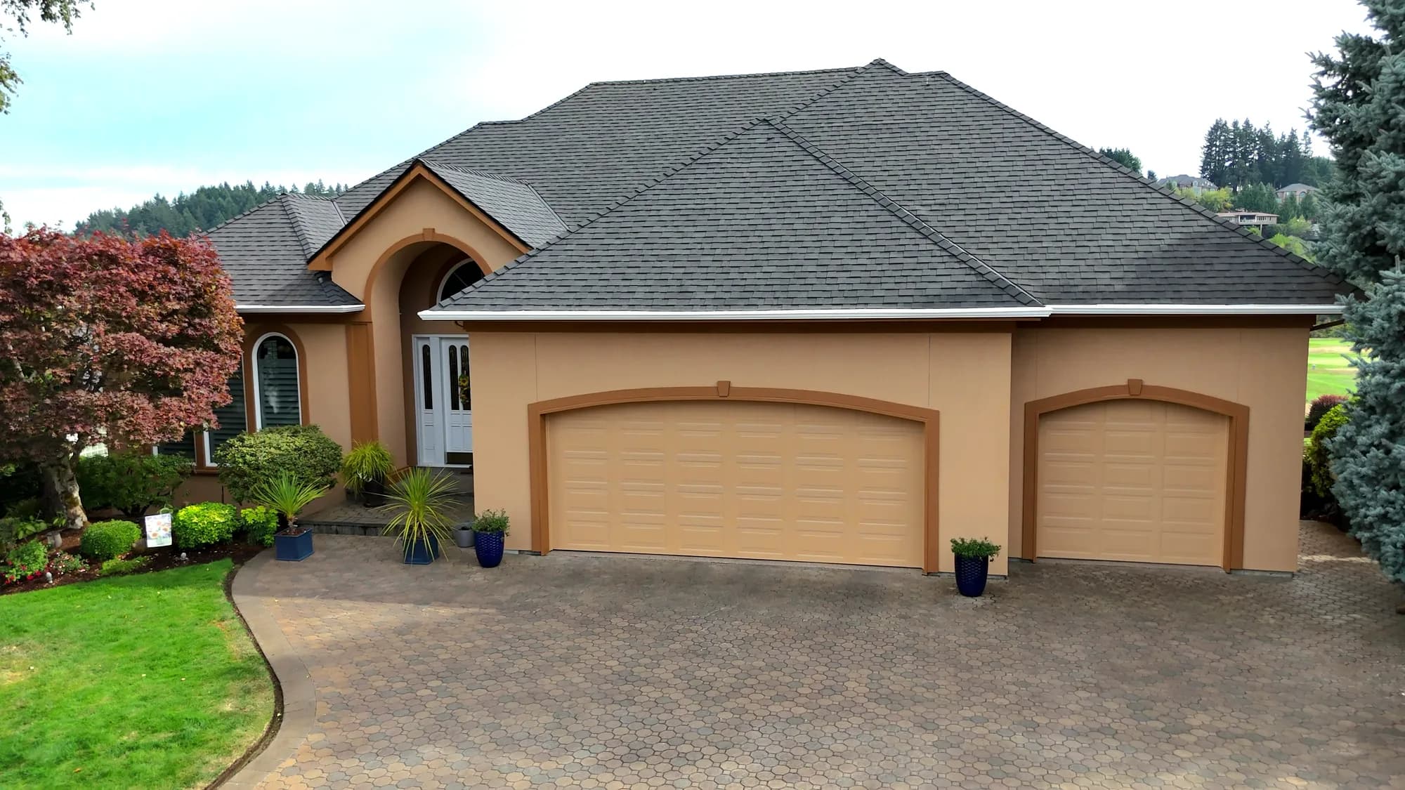Luxury tan stucco home with arched entry, three-car garage and circular paver driveway