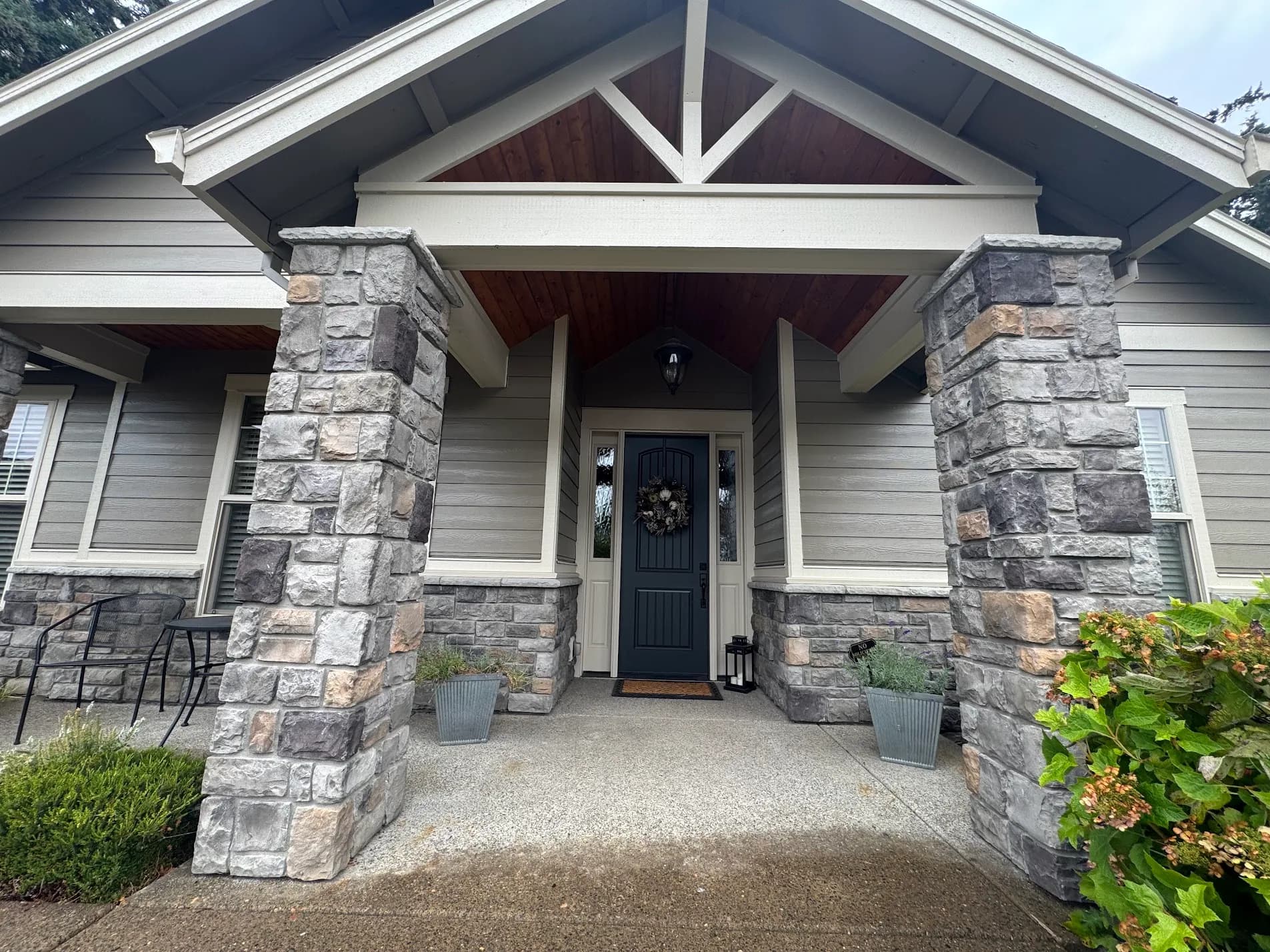 Covered craftsman entry with stone columns, stained cedar ceiling and dark blue front door