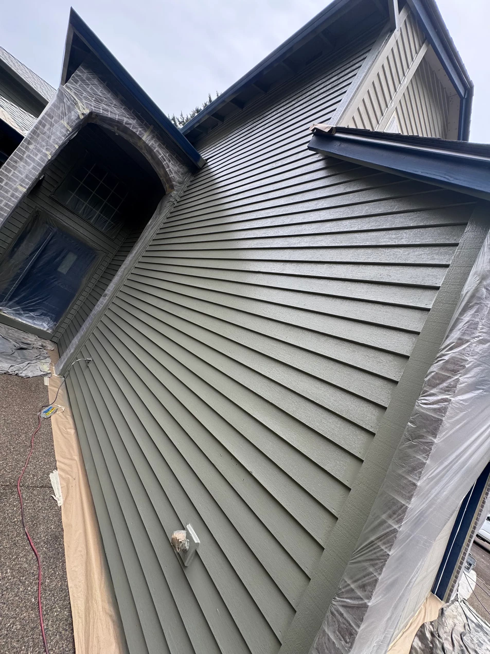 Masked and prepped home exterior mid-project showing plastic sheeting over windows and brick