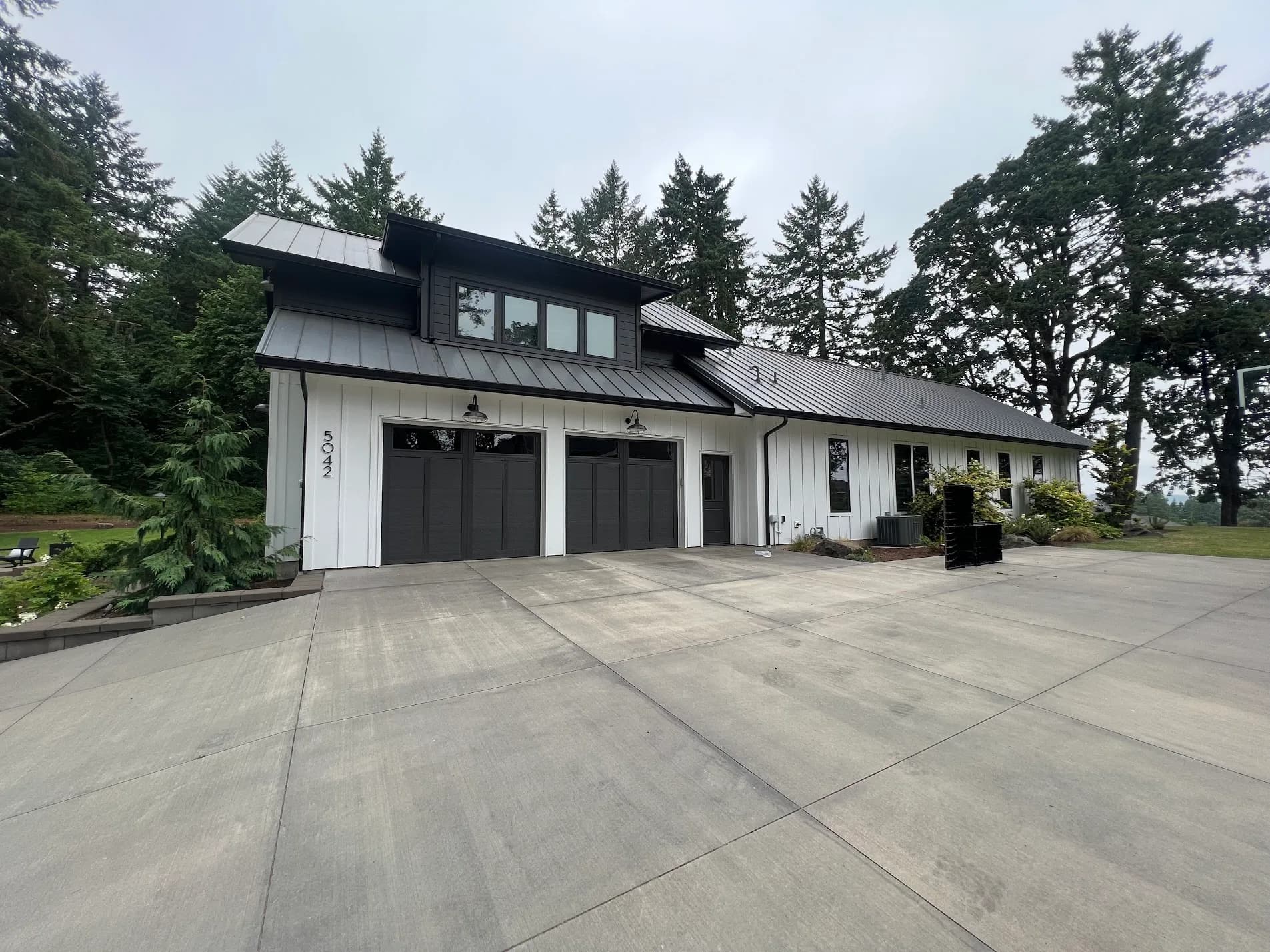 Modern black and white farmhouse with metal roof and dark garage doors after exterior painting