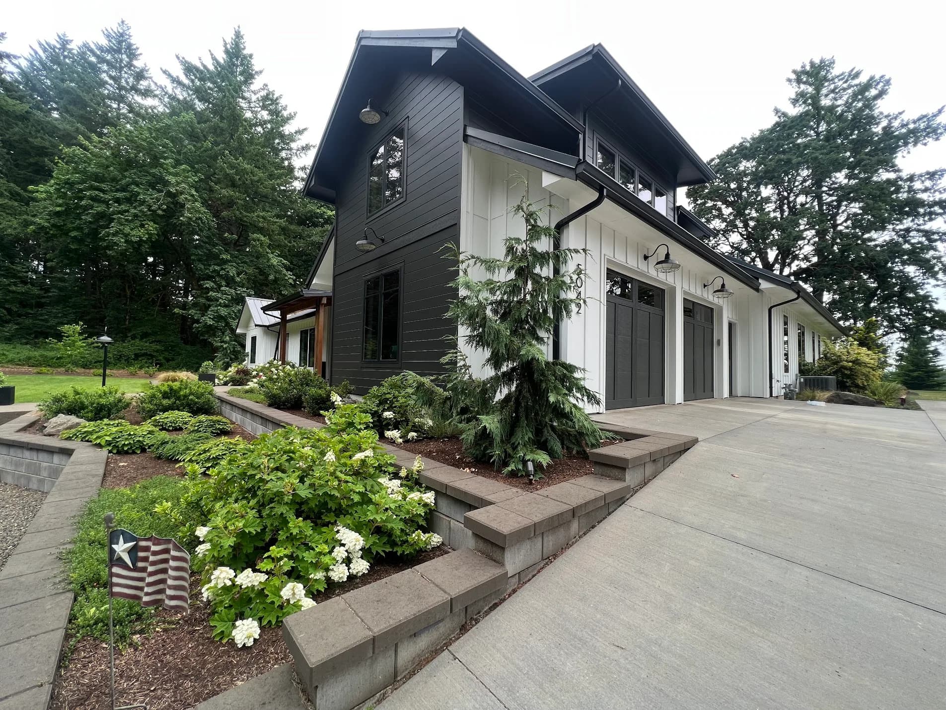 Side elevation of a modern black and white farmhouse with board and batten siding and landscaping